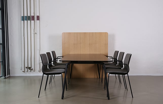 A table with a office screen divider attached to it and chairs in an empty room.