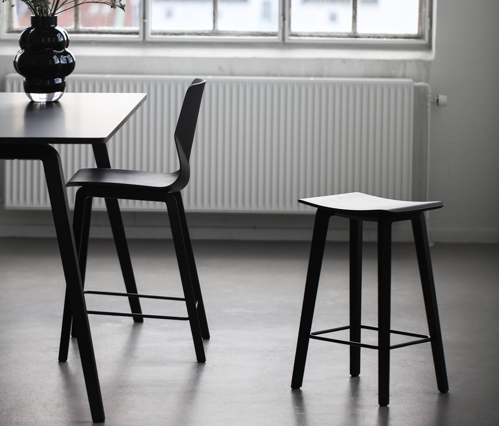 A dining table with two black counter height chairs and a stool in front of a window.
