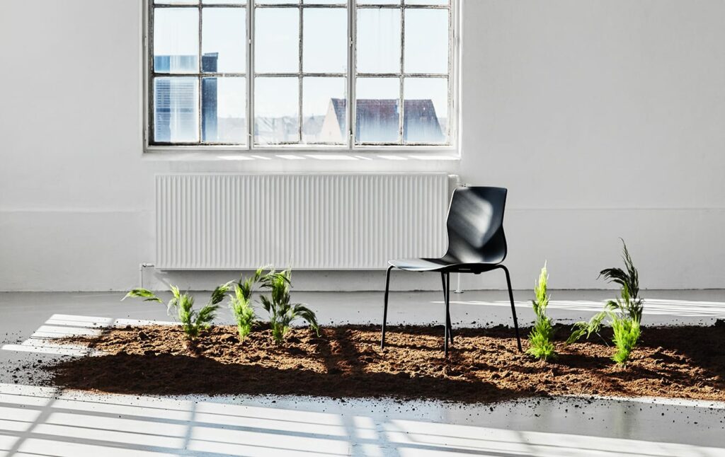 A black chair sits in the dirt next to a window.