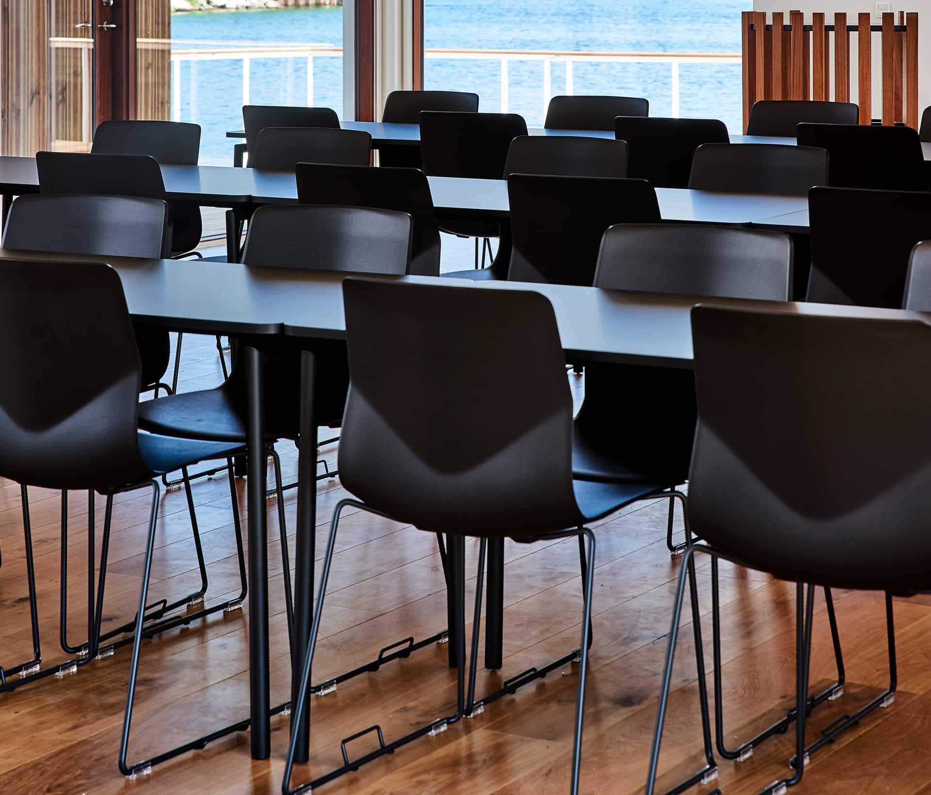 A long table with black chairs and a view of the water.