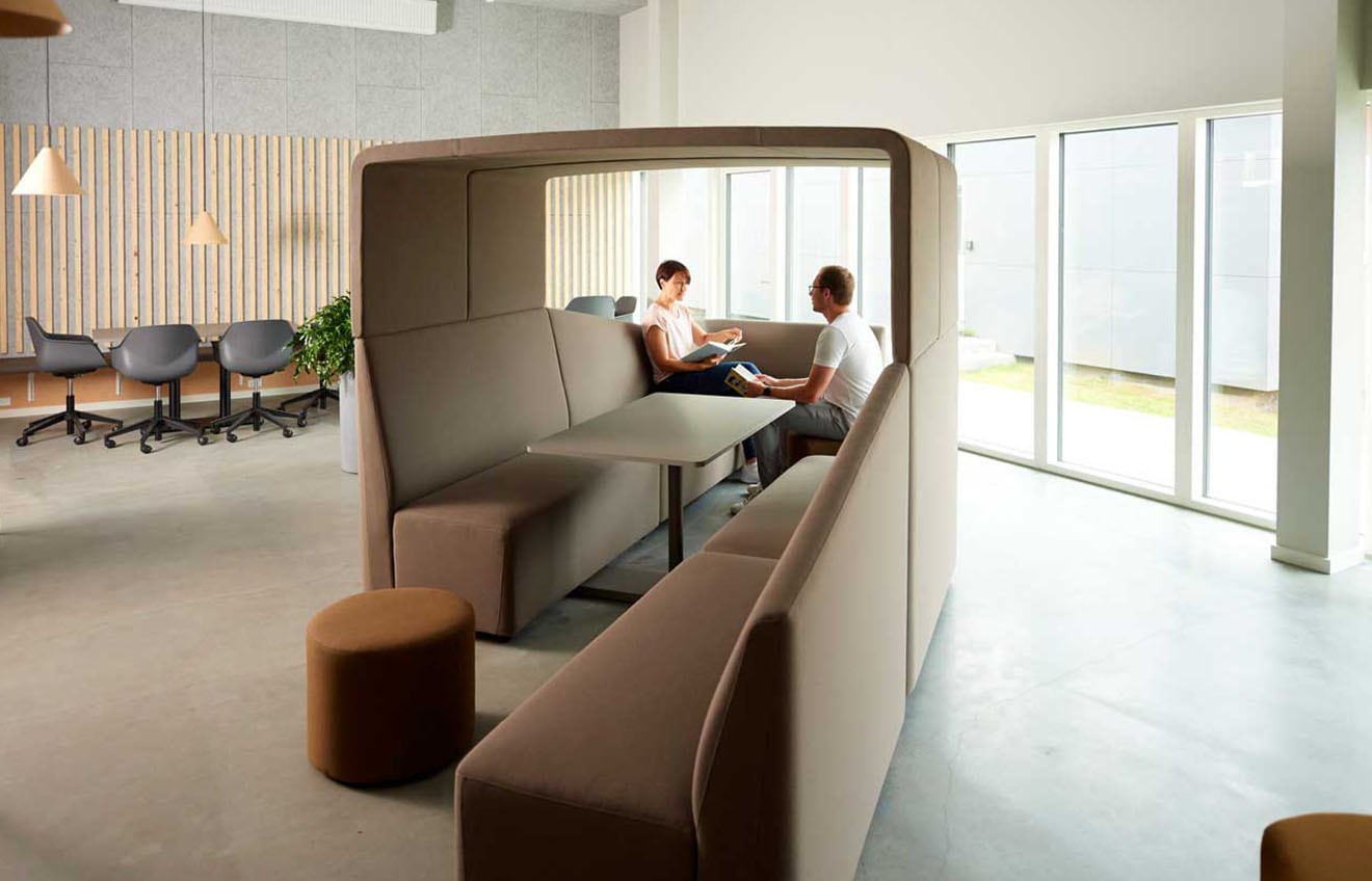 Two people sitting at a table in an office work booth in an office.