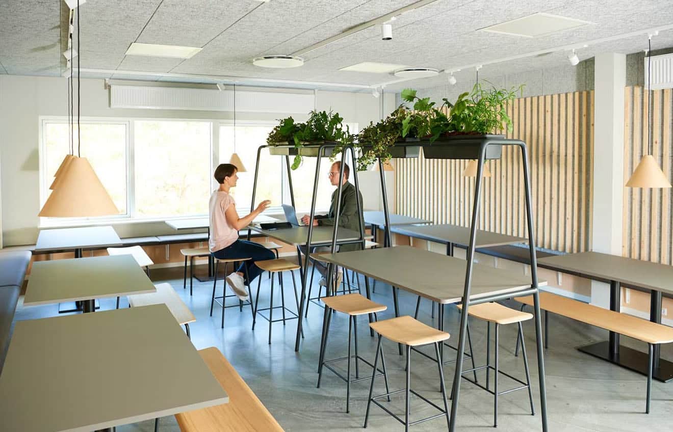 Two people are sitting at a table in an office filled with community tables, office tables and office stools