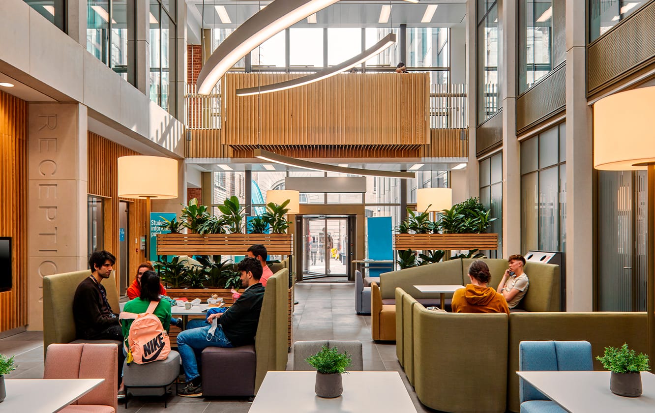 A group of people sitting at tables and on modular seating office sofas in a lobby.