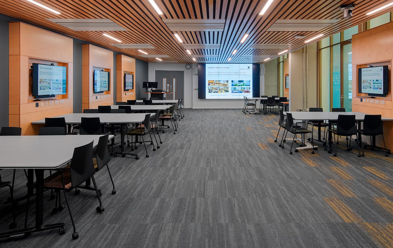 A room with office tables and office chairs and a projector screen.