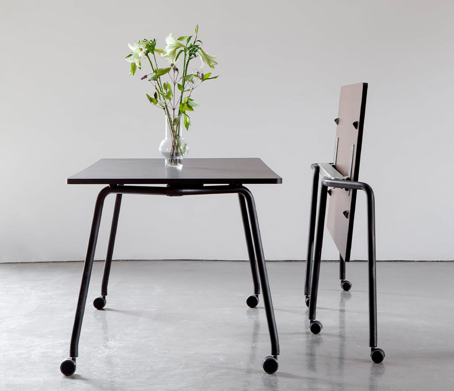 A table on wheels with a vase on it next to a folded table