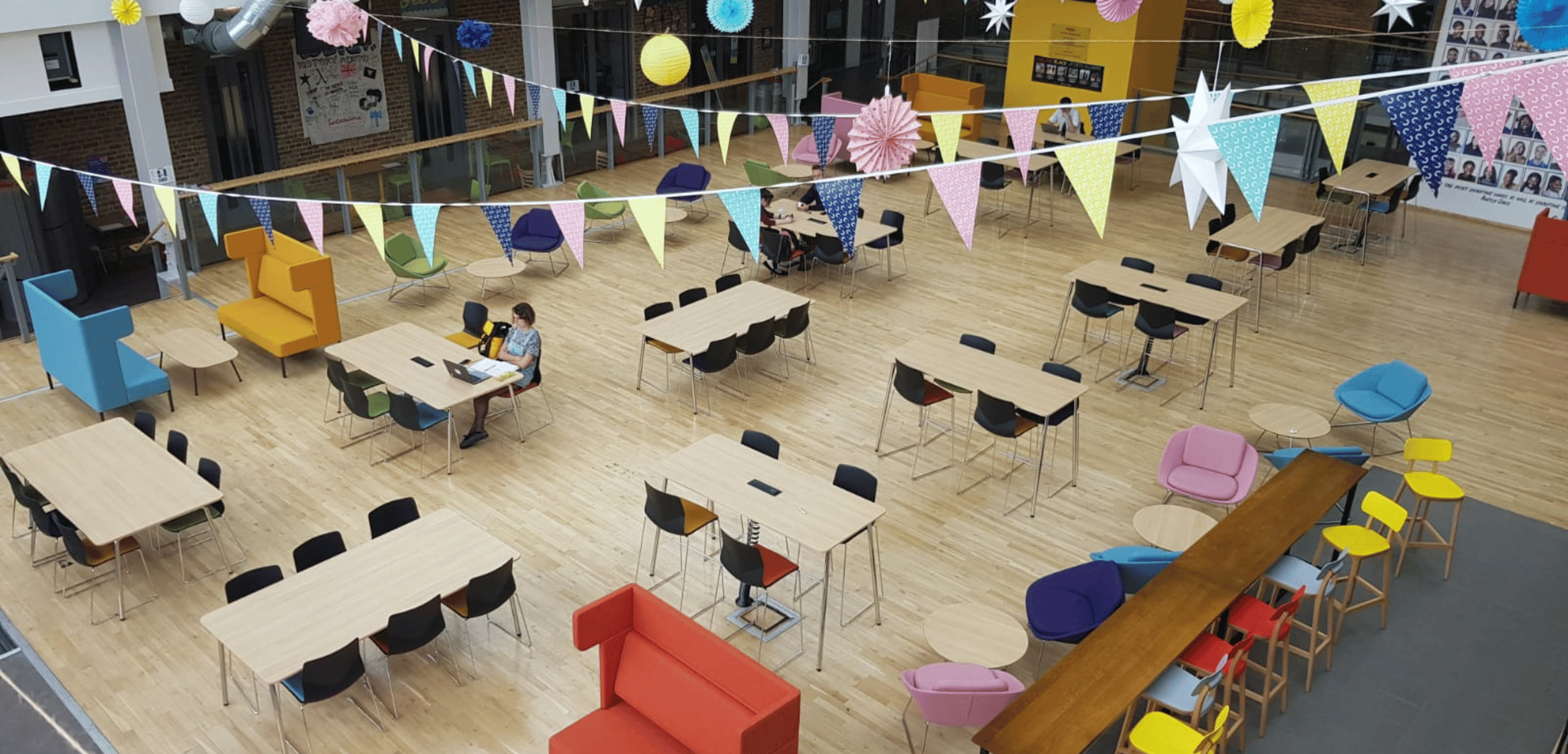 A large open space with colourful tables and chairs and office seating.