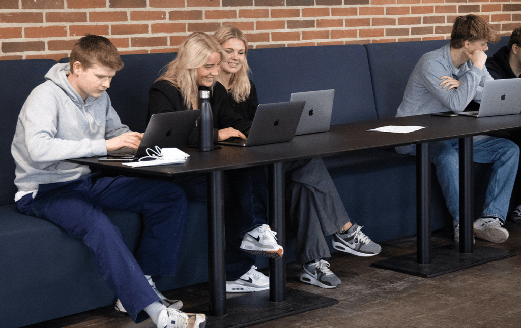 A group of people sitting at desk workstations using laptops.