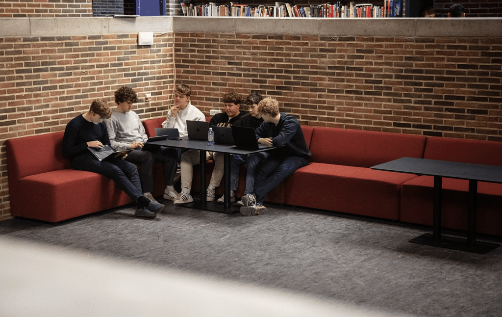 A group of people sitting on modular seating office sofas at desk workstations using laptops.