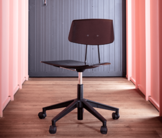 A Share Move black office chair without arms in front of a pink wall.