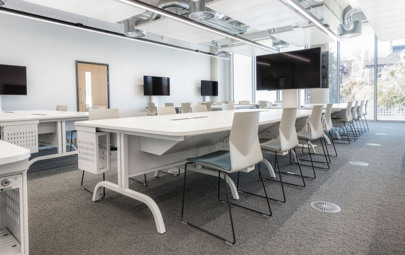 A classroom with tables and chairs and a tv with Ocee and Four Design office furniture as part of our student centre design for the University of Sheffield