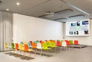 A conference room with colorful chairs and a projection screen with FourSure 88 office desk chairs in it.