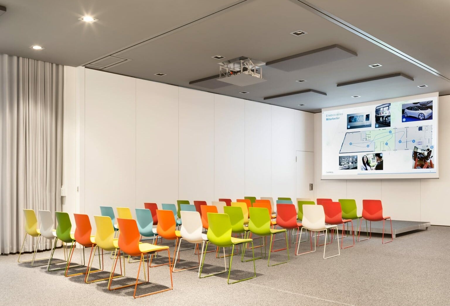 A conference room with colorful chairs and a projection screen with FourSure 88 office desk chairs in it. 