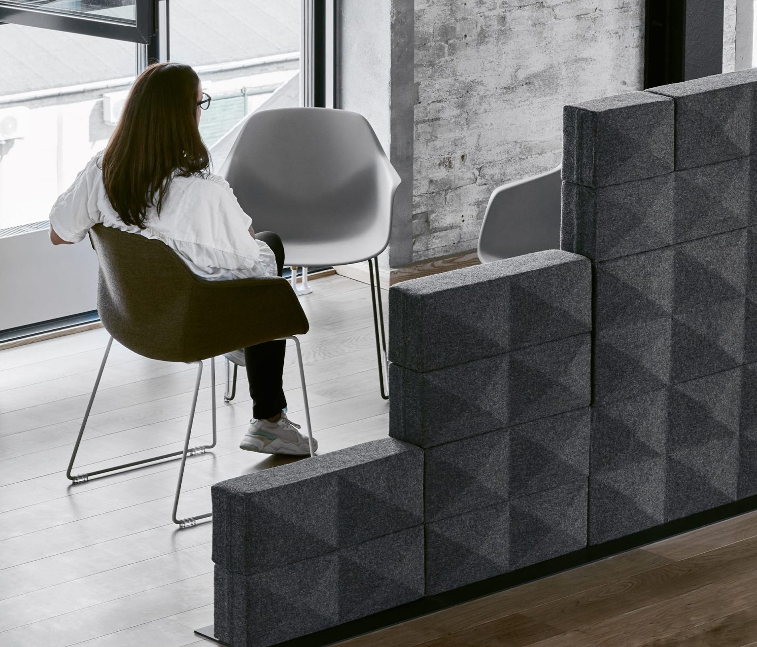 A woman sits in a chair in front of a gray wall of Fabricks FourMe 88 office acoustic solutions