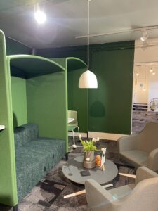 Den office work booths with a green couch and chairs.