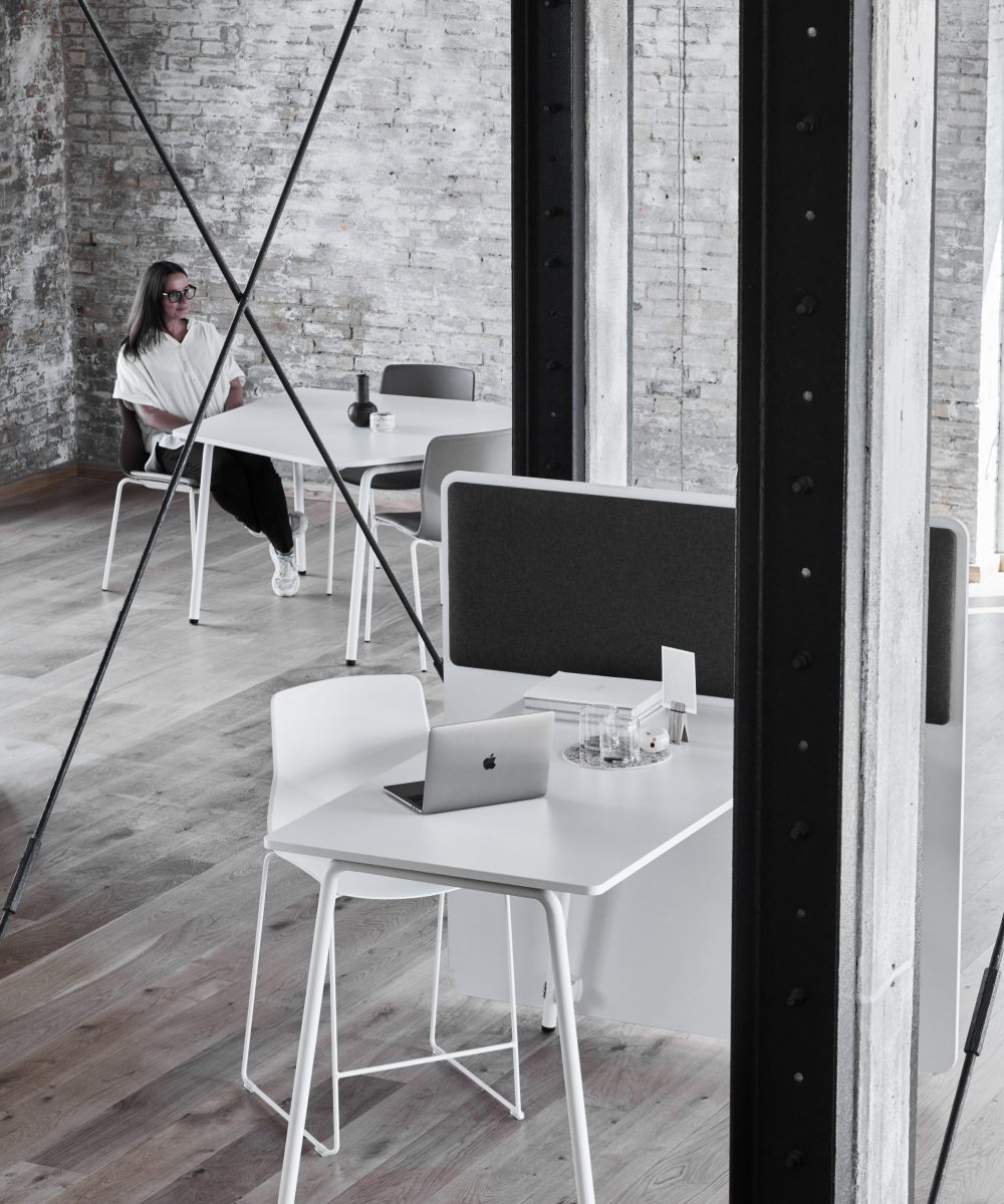 A white FourReal 90 table in the foreground with a white FourSure 44 chair with a lady in the background at a FourReal 90 table