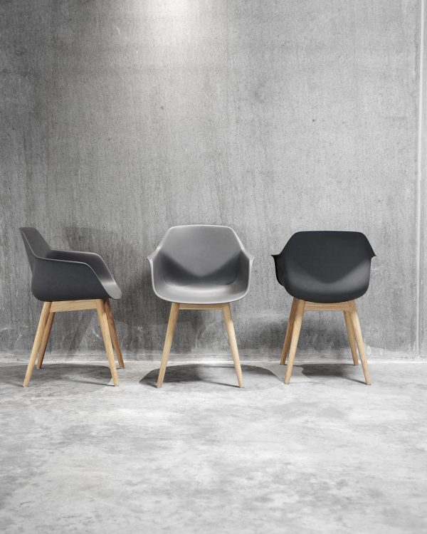 Three grey chairs with wooden legs in front of a concrete wall.
