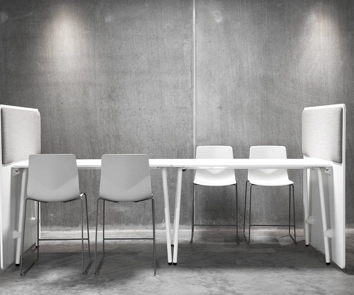 A white table with office screen dividers and chairs in a concrete room.