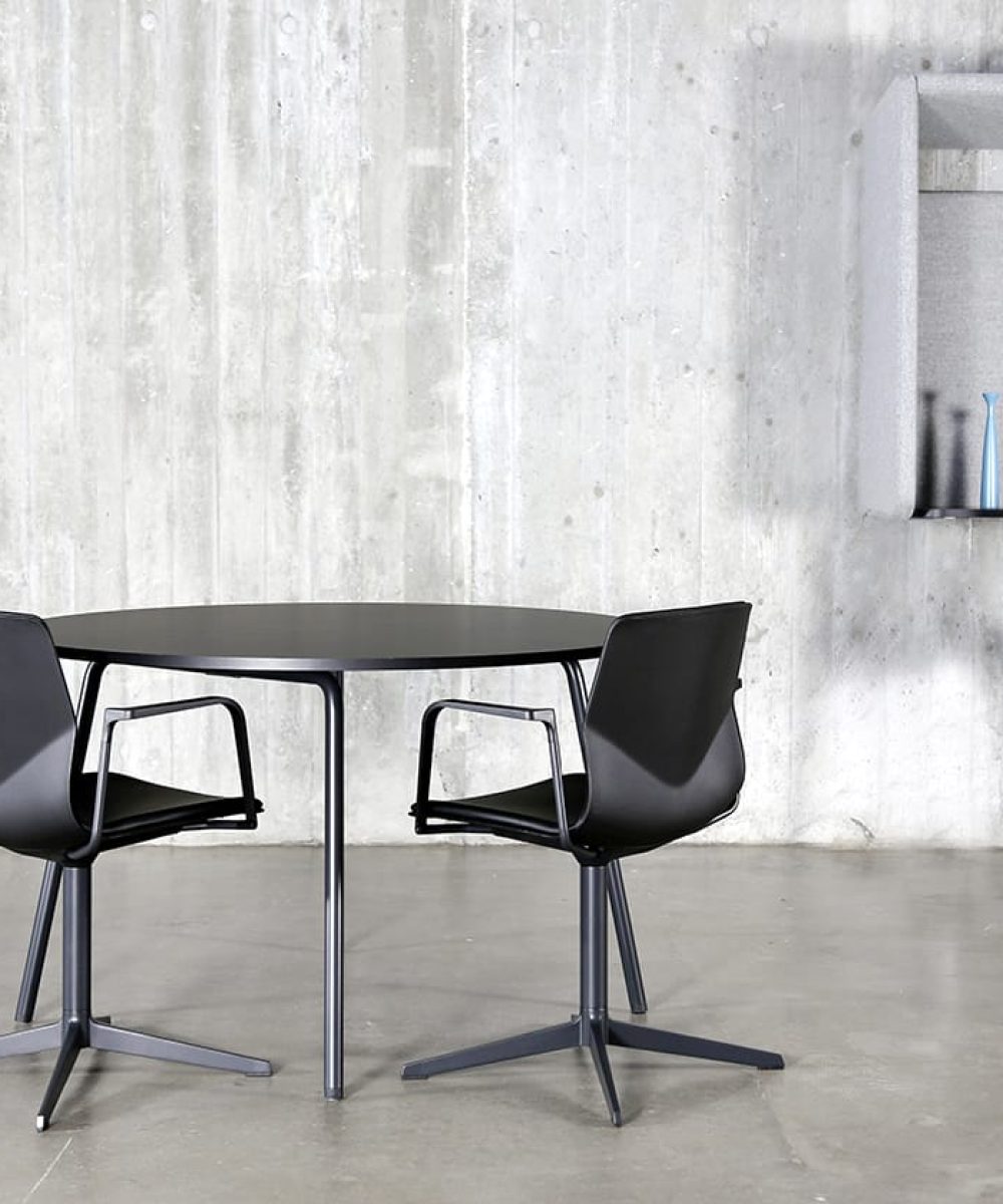 Four chairs and a table in a room with a wall mounted desk workstation on a concrete wall.