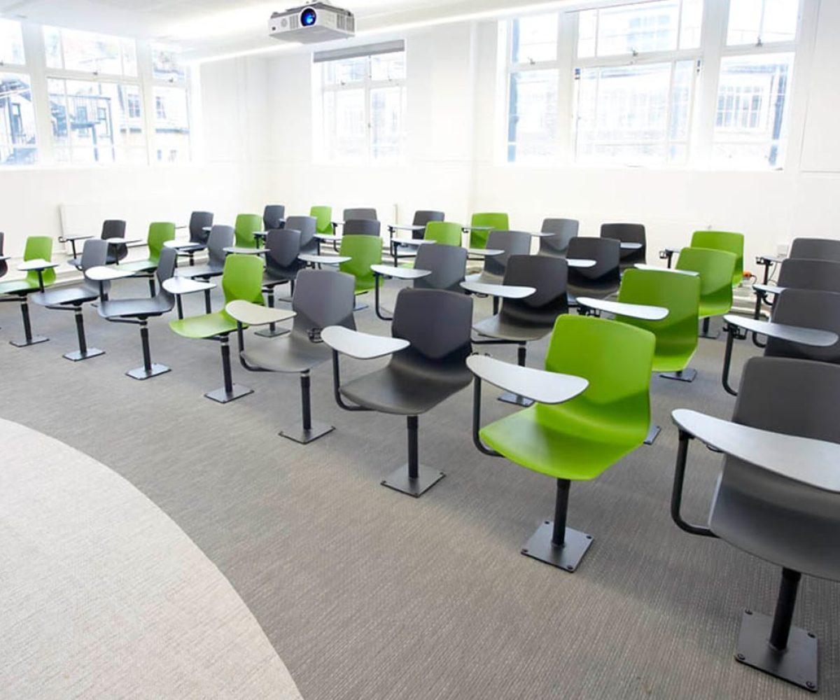 A classroom with green chairs with desk attached and a projector