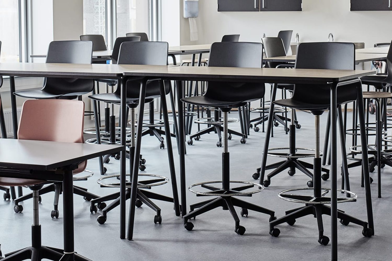 A classroom with a lot of office desk chairs and standing height tables.