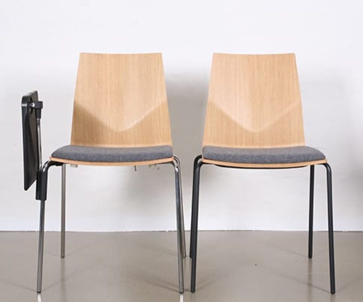 Two wooden chairs with a grey upholstered seat. One has a desk attached that is folded down