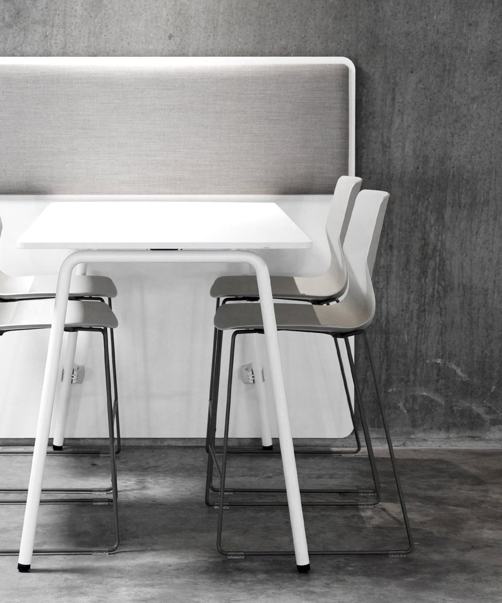 A white table with office screen dividers attached and chairs in a concrete room.