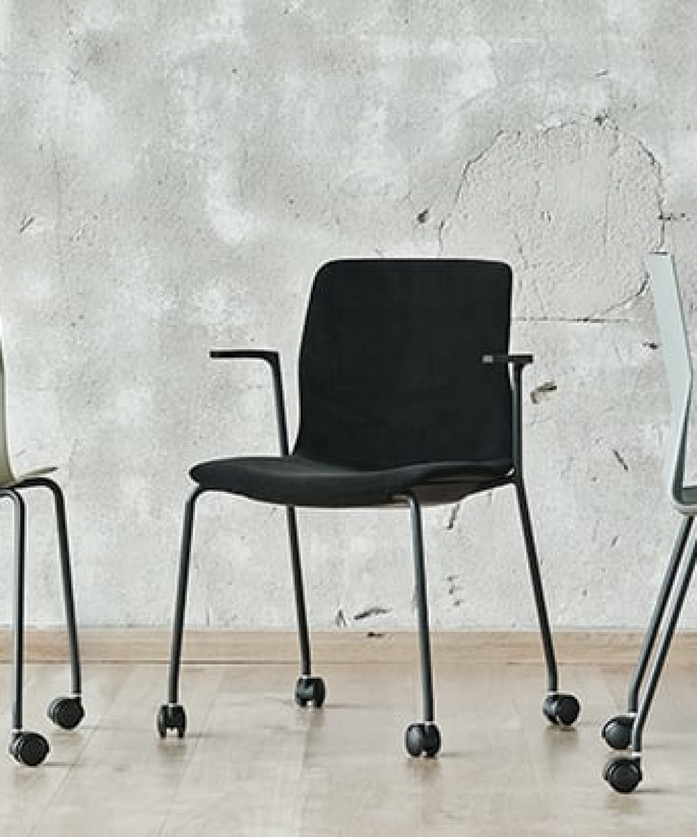 Three office desk chairs on wheels in front of a wall.